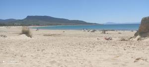 a beach with people sitting on the sand and the water at Apartamentos Bolonia - M a n u e l a in Bolonia