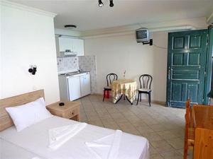 a room with a bed and a kitchen with a table at kirki rooms in Armenistis