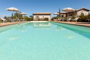ein großer Pool mit blauem Wasser, Stühlen und Sonnenschirmen in der Unterkunft Agriturismo Colle Oliveto in Orbetello
