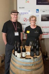 a man and a woman standing next to a barrel of wine at Judge Rock Exclusive Vineyard Cottage Accommodation in Alexandra