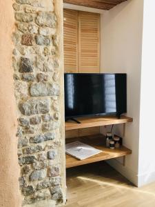 une télévision assise sur un support en bois à côté d'un mur en pierre dans l'établissement Le Salon de l'Isle, à Carentan