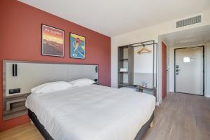 um quarto com uma grande cama branca e paredes vermelhas em Kyriad Bordeaux Nord Sainte Eulalie em Sainte-Eulalie