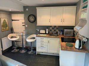 a kitchen with white cabinets and two bar stools at Thatched Cottage in Pulborough