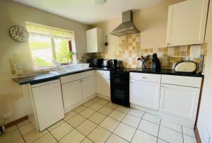 cocina con armarios blancos, fregadero y ventana en Derrybrook Cottage, Twin or Superking, Seven Springs Cottages, en Cheltenham