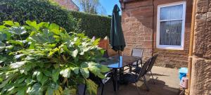un patio con mesa, sombrilla y plantas en Criffel Cottage, en Dumfries