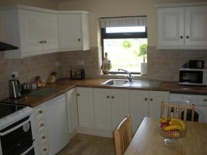 una cocina con armarios blancos y un bol de fruta en una mesa en Beautiful 3-Bed House in Knock, en Knock