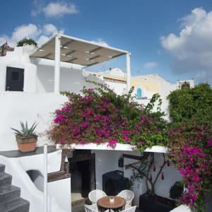 a white building with purple flowers and a table and chairs at Villa Orpheus Santorini in Megalokhori