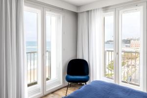 a bedroom with a blue chair in front of windows at Hôtel Le Windsor Biarritz in Biarritz