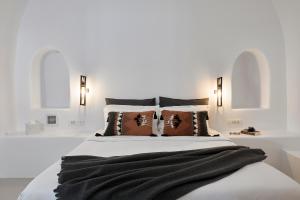 a white bedroom with a large bed with pillows at Blue Art Caves in Oia +38 photos
