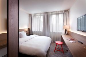ニュルンベルクにあるゾラート ホテル ザックス ニュルンベルクの白いベッドと赤いスツールが備わるホテルルームです。