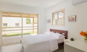 a white bedroom with two beds and a window at Tal Shahar Zimmers in Tal Shaẖar