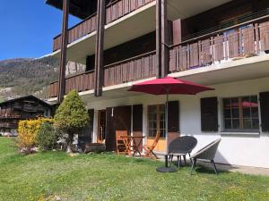 un patio con 2 sillas y una sombrilla frente a un edificio en Le Cerf, magnifique studio avec jardin-terrasse et garage, en Evolène