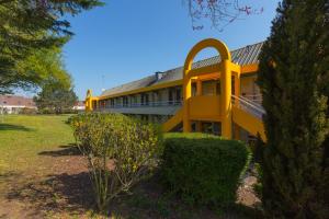 a yellow building in a park with trees and bushes at Premiere Classe Chantilly Sud Luzarches in Chaumontel
