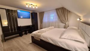 a bedroom with a large white bed and a flat screen tv at Pensiunea Mădălina in Durau