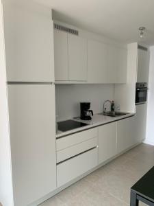 a white kitchen with white cabinets and a sink at Nieuwbouwappartement Lippenslaan, 2 -Slaapkamers Geen Groepen Jongeren in Knokke-Heist