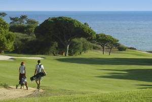 two people and a dog walking on a golf course at Sunny Acacia Apartment in Vale do Lobo