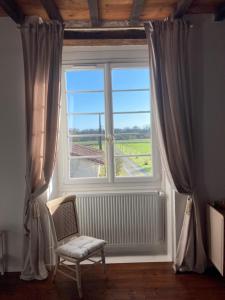 une fenêtre avec une chaise et une vue sur un champ dans l'établissement L'Intemporelle, à Ozourt