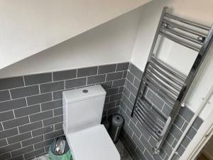 a bathroom with a white toilet and a gray tiled wall at Charming Town Centre Character Cottage With Parking in Stowmarket