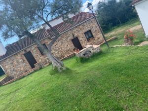 ein altes Steinhaus in einem grünen Garten mit einem Baum in der Unterkunft Finca La Portilla in Aroche