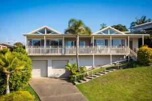 a large white house with a porch and a palm tree at Pelican Lake Holiday House in Merimbula