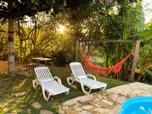 two white chairs and a hammock in a yard at Casa com piscina fundo pra represa e AR Condicionado CasinhaBrancaDeVaranda in Ijaci