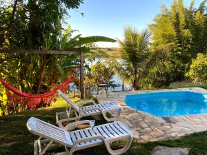 deux chaises et un hamac à côté d'une piscine dans l'établissement Casa com piscina fundo pra represa e AR Condicionado CasinhaBrancaDeVaranda, à Ijaci