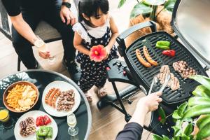 a little girl standing next to a grill with food at Nest Hotel Naha Kumoji in Naha