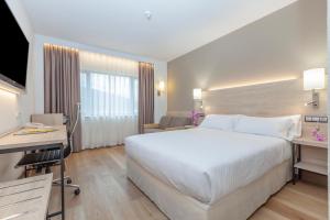 um quarto de hotel com uma grande cama branca e uma secretária em Hotel Puerta de Bilbao em Barakaldo