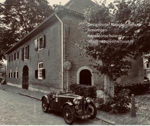 een oude auto geparkeerd voor een bakstenen gebouw bij Hotel Napoleonschuur in Amerongen