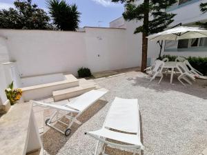 eine Terrasse mit weißen Stühlen, einem Tisch und einem Sonnenschirm in der Unterkunft Residence Leucasia in Santa Maria di Leuca
