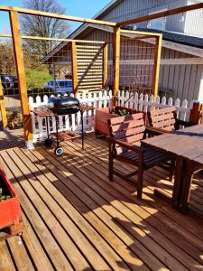 a wooden deck with a grill and tables and benches at Lillstugan - Centralt och havsnära i lugnt villområde in Falkenberg