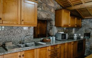 a kitchen with wooden cabinets and a sink and a microwave at Casas da Peneda - Geres in Gavieira