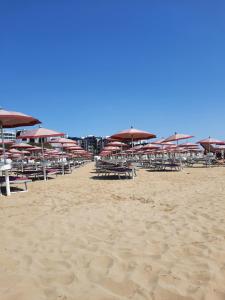 einen Strand mit Tischen und Sonnenschirmen auf dem Sand in der Unterkunft Hotel Villa Dina in Lido di Jesolo