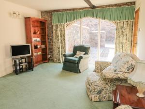 uma sala de estar com um sofá e uma cadeira e uma televisão em Lupin Cottage em Wooler