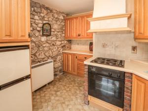 a kitchen with a stove and a stone wall at Lupin Cottage in Wooler