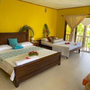 een slaapkamer met 2 bedden en een gele muur bij Linsen Selfcatering Apartments in La Digue