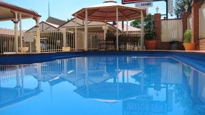a swimming pool with an umbrella and some chairs and tables at Dalby Mid Town Motor Inn in Dalby