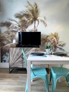 a table with chairs and a tv on a wall with palm trees at Nos Îles in Saint-Jean-de-Monts