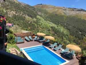 a swimming pool with chairs and umbrellas next to a mountain at Refúgio Muas Nature in Vila Real