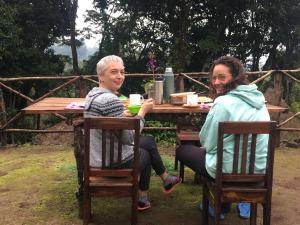 zwei Personen sitzen an einem Holztisch mit in der Unterkunft Mai Kilimanjaro Home Stay in Marangu