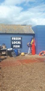 a sign that reads fresh local fish next to a blue building at Beautiful Spacious Holiday Home - Romney Sands in New Romney