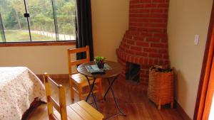 a bedroom with a table and a brick fireplace at Pousada Leal Chalé in Visconde De Maua