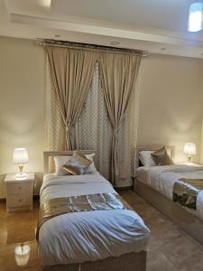 a bedroom with two beds and a window with curtains at المبيت للشقق الفندقية in Sirr Āl Ghalīz̧