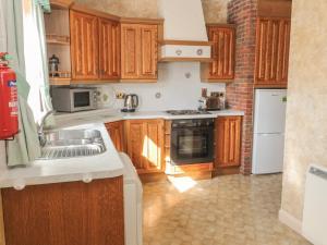 a kitchen with wooden cabinets and a sink and a stove at Honeysuckle in Wooler