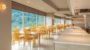 a dining room with tables and chairs and windows at Akazawa Onsen Hotel in Ito