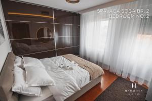 um quarto com uma cama com lençóis brancos e almofadas em Harmony Apartmani Arandjelovac em Arandjelovac