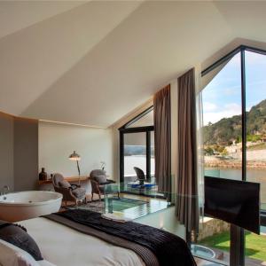 a bedroom with a tub and a large window at Douro Suites in Riba Douro