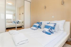 a white bed with blue pillows and a mirror at Marina Primore Apartments by Renters in Gdańsk