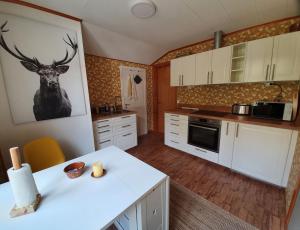 a kitchen with white cabinets and a deer picture on the wall at Ferienwohnung Lövåsängen im Waldbauernhof, Årjäng in Årjäng