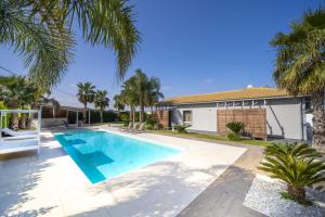 a swimming pool in front of a house with palm trees at Aqua Venere Pool & Suites in Marsala